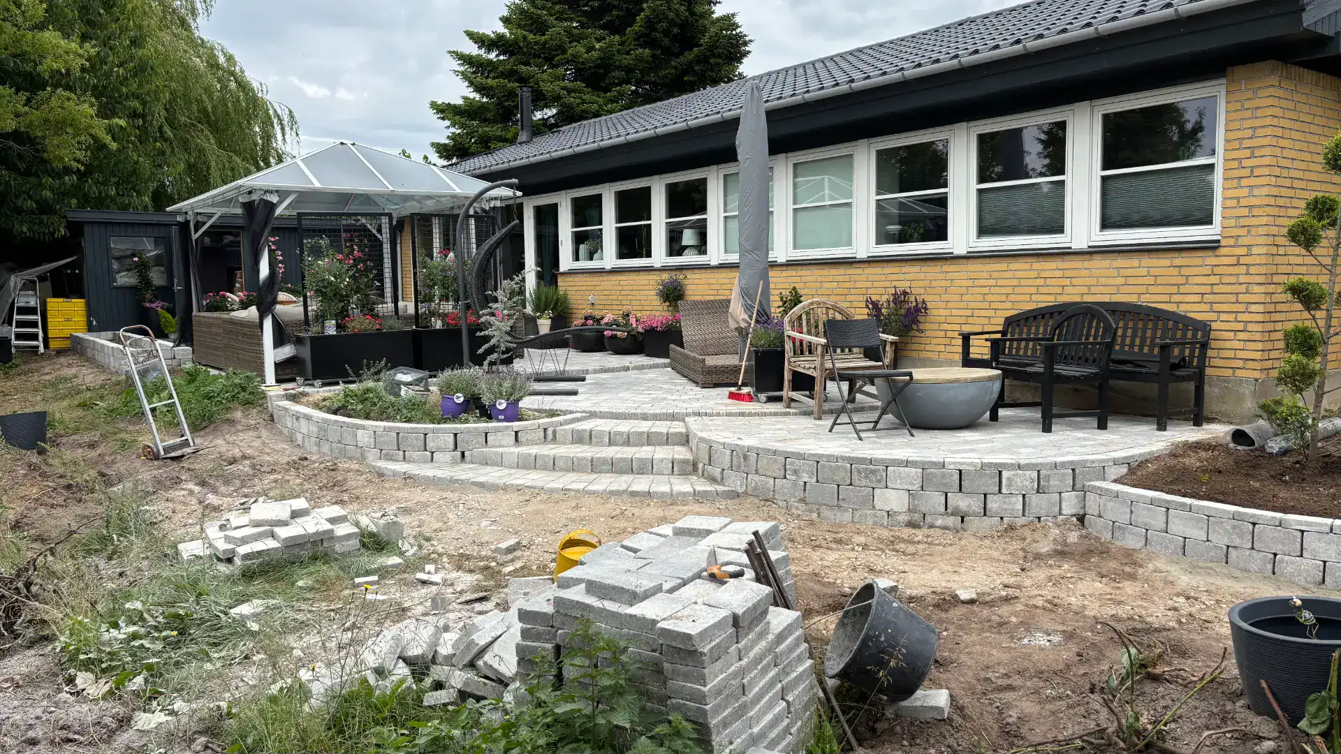 Udendørs terrassebyggeri med stenbelægning foran hus.