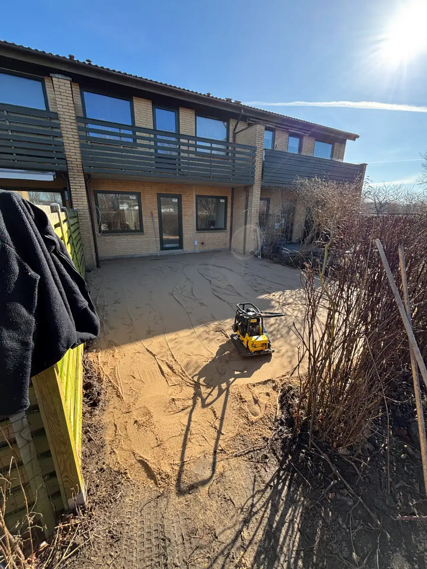 Udendørs byggeprojekt foran moderne bolig med værktøj og sand.
