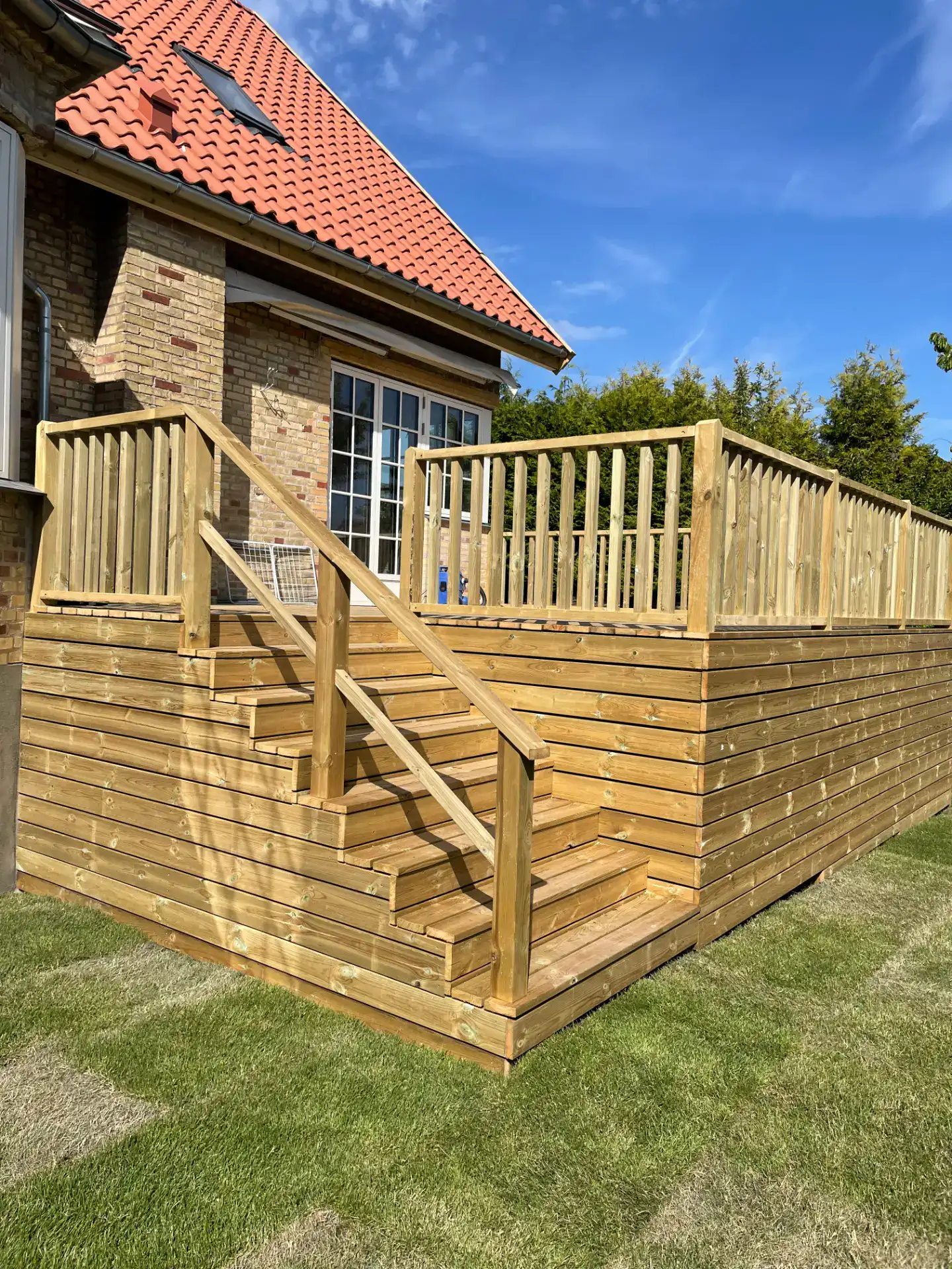 Terrasse med trætrappe og sikkerhedsgelænder foran huset.
