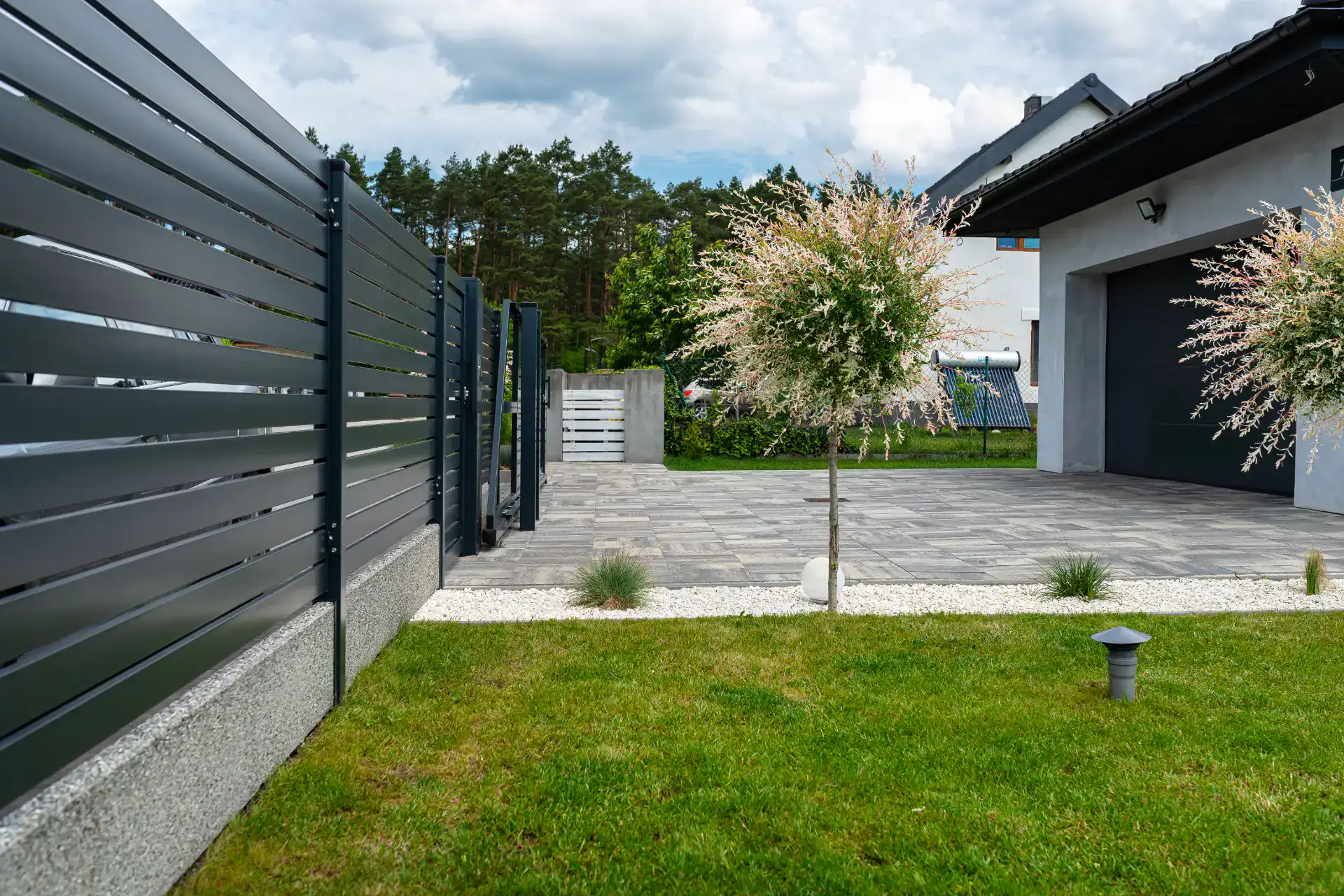Elegant indkørsel med stenfliser, moderne hegn og velplejet græsplæne.